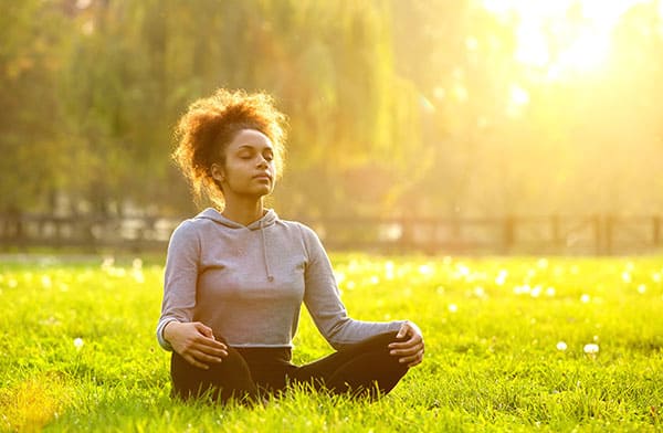 woman meditating in the grass with the sun shining